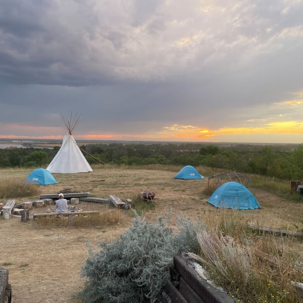 Campground in a grassy plain with multiple small blue camping tents and a large white tipi in the middle.