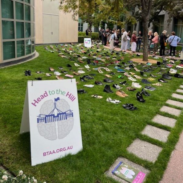 A large number of shoes sitting on a grass slope, behind a Head to the Hill sign
