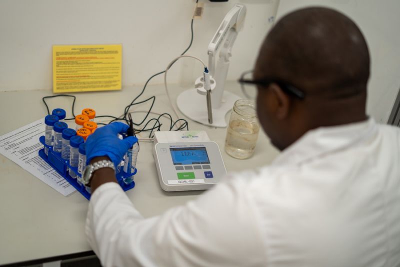 An over-the-shoulder shot of Simon at a work bench using equipment and glass test tubes
