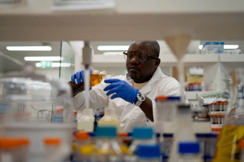 Simon pictured in a lab pouring a brown liquid sample into a test tube