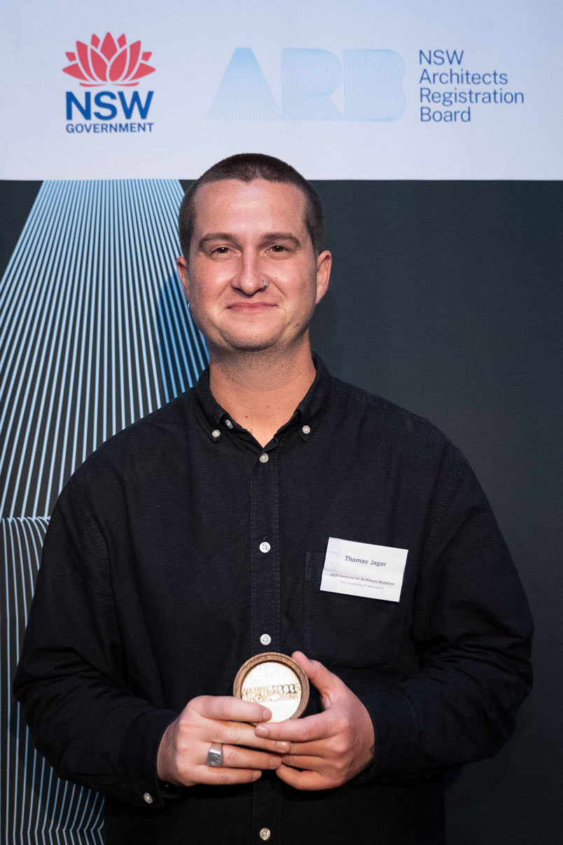 Thomas Jager stands in front of a NSW Architects Registration Board Banner, holding his Medallion