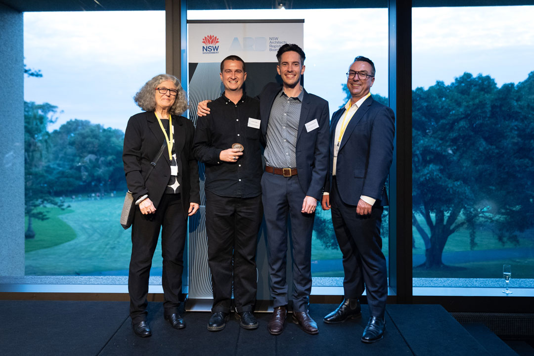 Thomas Jager holds his medallion, and stands with Dr Timothy Burke, and two other individuals. They are all smiling, standing on the stage at the award presentation night.