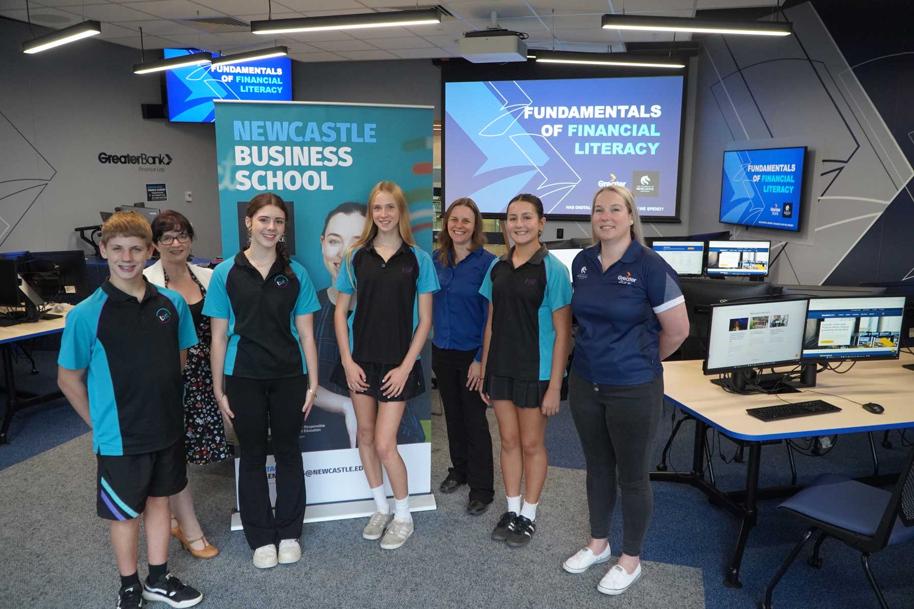 Four high school students, one University of Newcastle academic and two Greater Bank representatives standing together, looking directly at the camera and smiling.