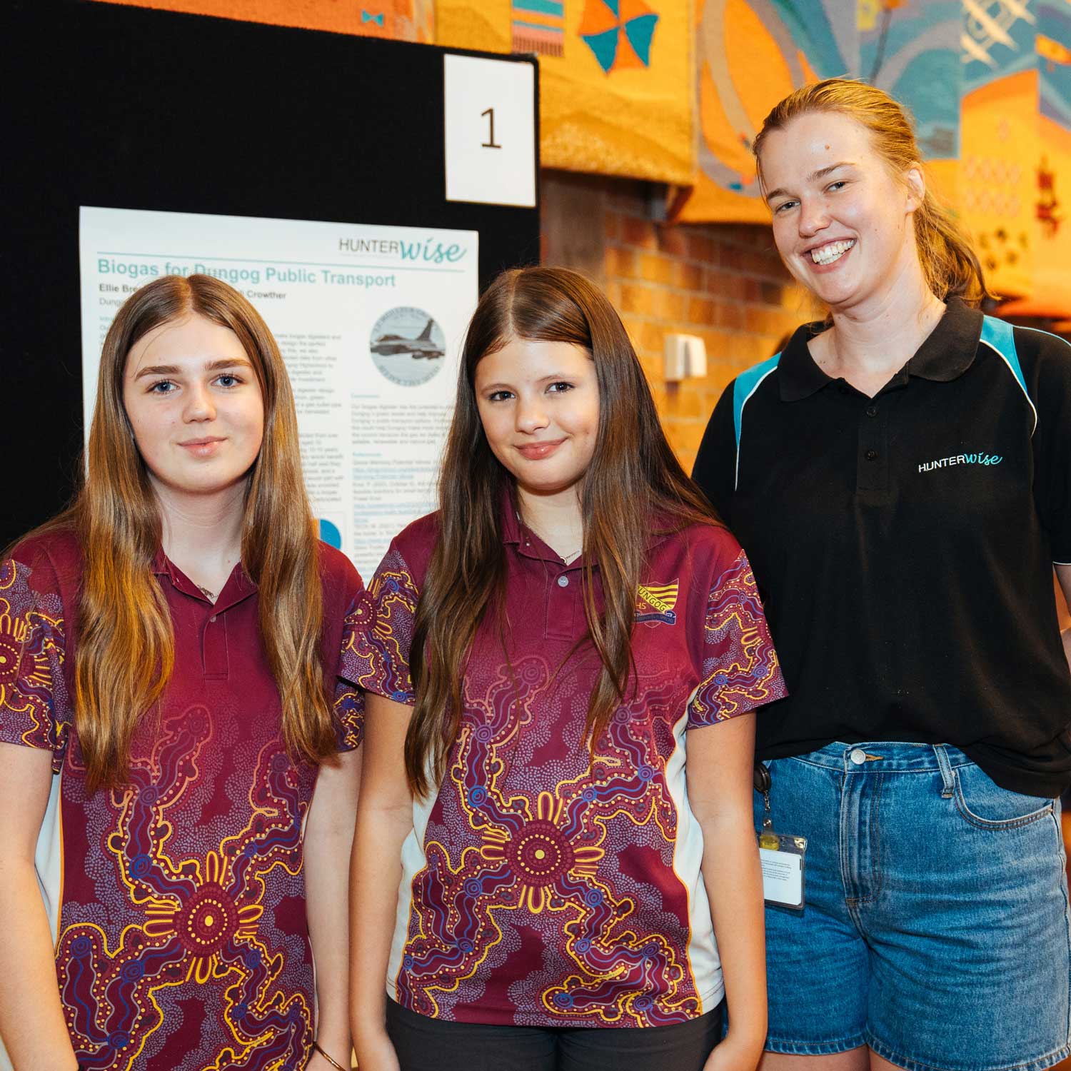 Two students from Dungog High School wearing their burgundy uniform t-shirts featuring Aboriginal artwork, standing with their HunterWISE mentor, a blonde female wearing a black t-shirt.