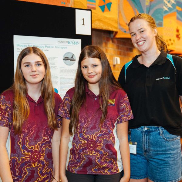 Two students from Dungog High School wearing their burgundy uniform t-shirts featuring Aboriginal artwork, standing with their HunterWISE mentor, a blonde female wearing a black t-shirt.. Creating Confidence in STEM for Girls.