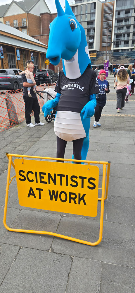 Hunter the Mascot standing infront of scientits at work sign