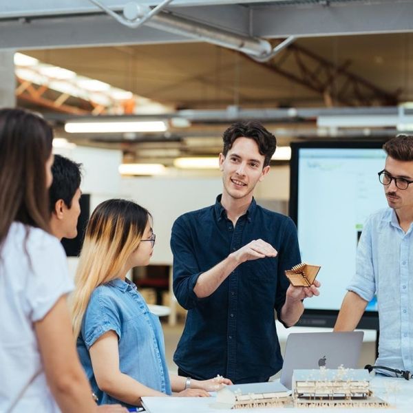 5 students standing at a table, with one student showing an object