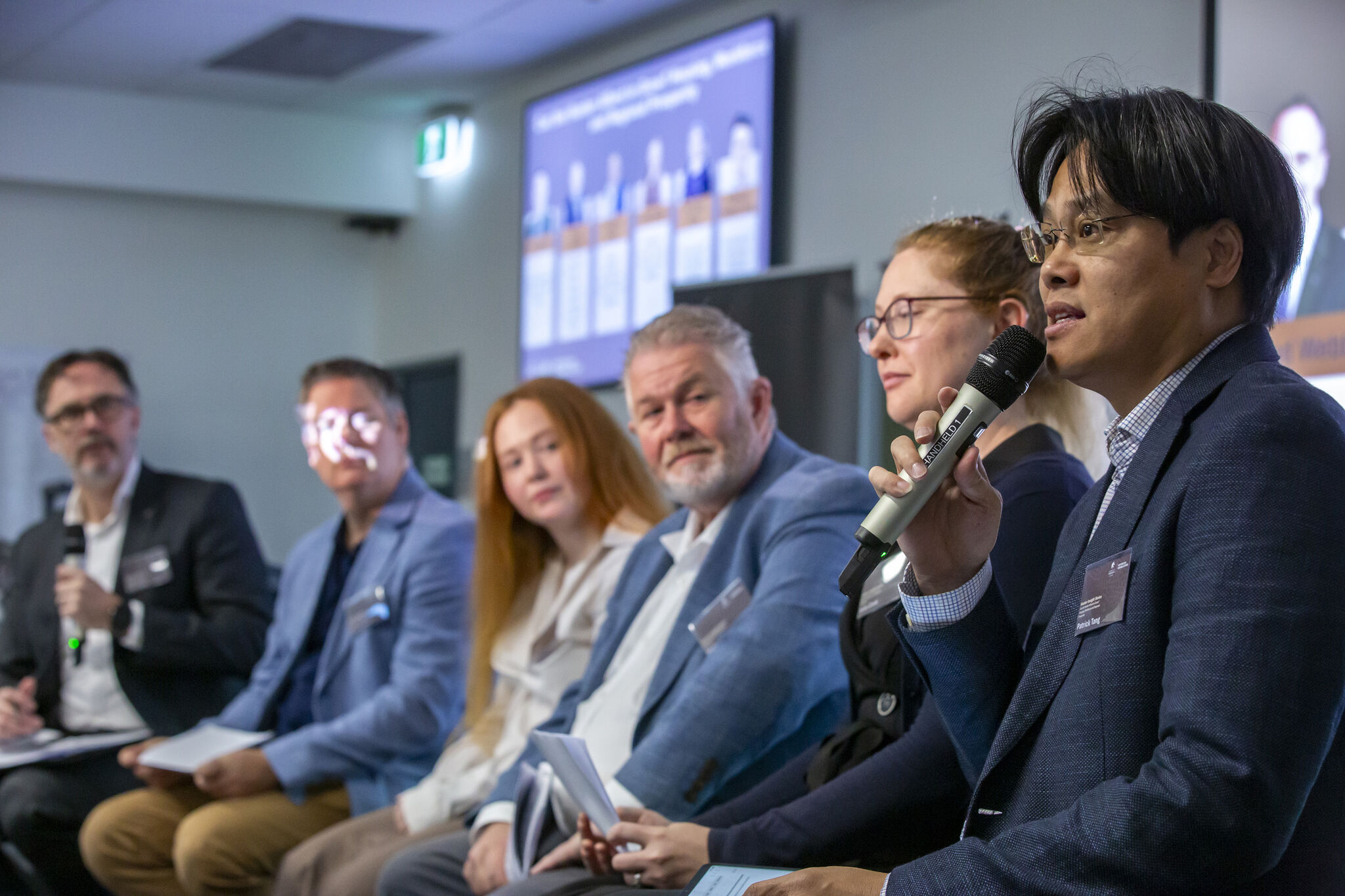 Group of people sitting on chairs with one person talking into a microphone