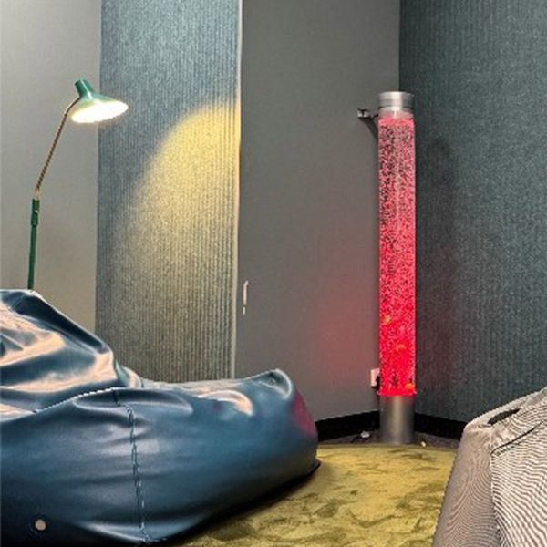 A blue bean bag sits on top of a yellow rug. An over-head light is above the bean bag and a pink lava lamp is on the right.