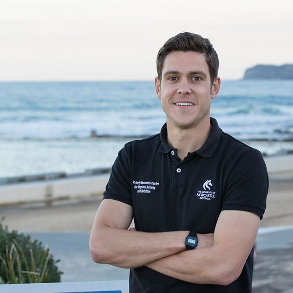 lee-ashton.jpg Dr Lee Ashton smiling in front of a beach, wearing a University of Newcastle shirt, arms crossed