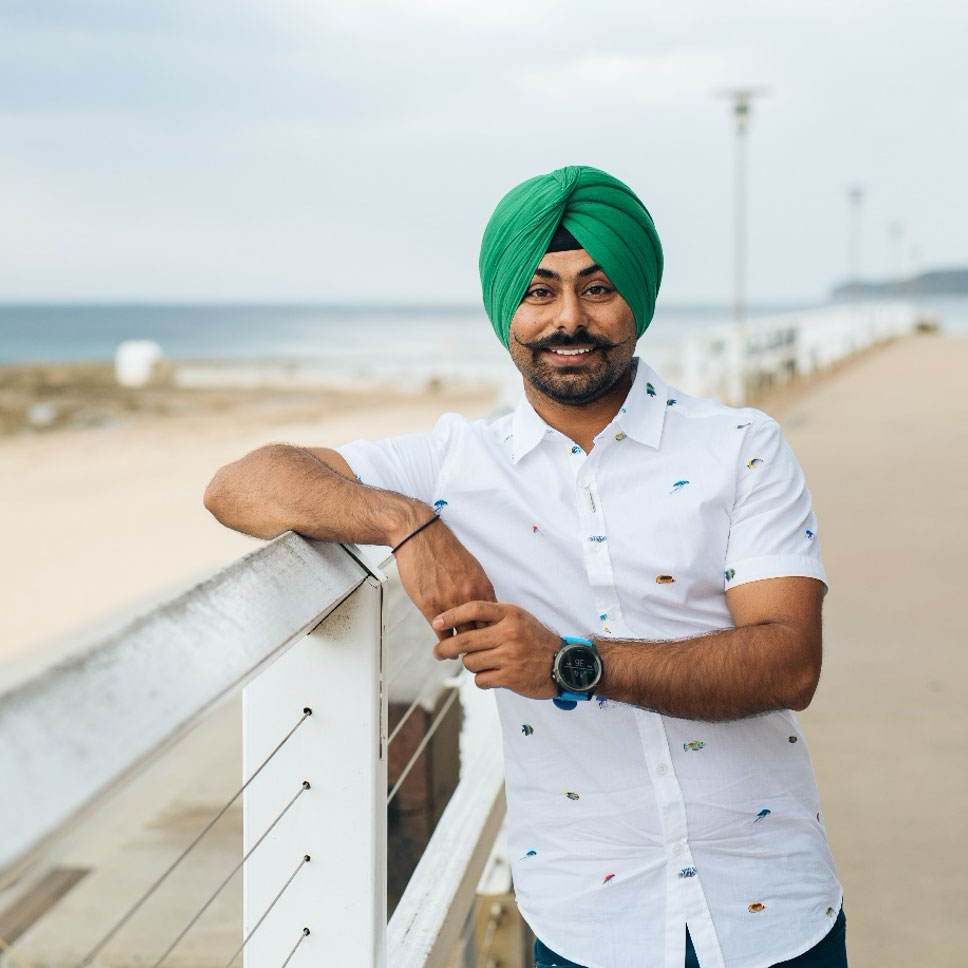 Harsimranjeet smiling, leaning on fence at beach