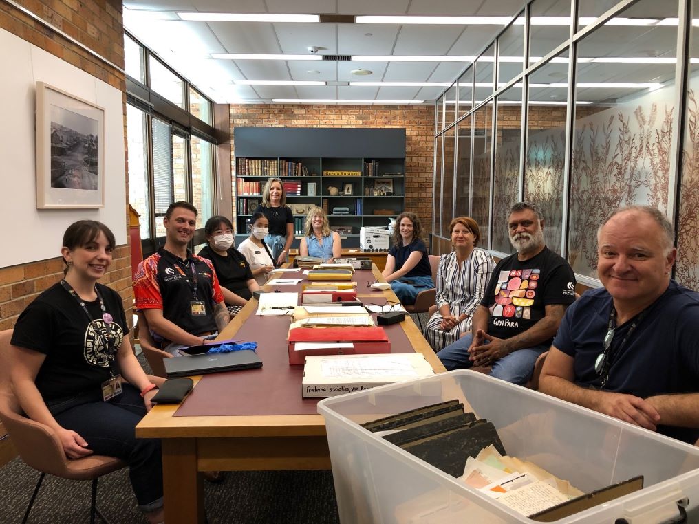 A group of people sitting around a long table covered with files and papers