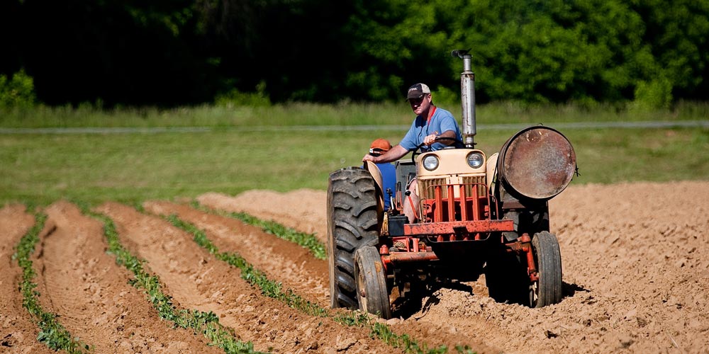 A man sits on a tractor looking down at the dry ground below him.