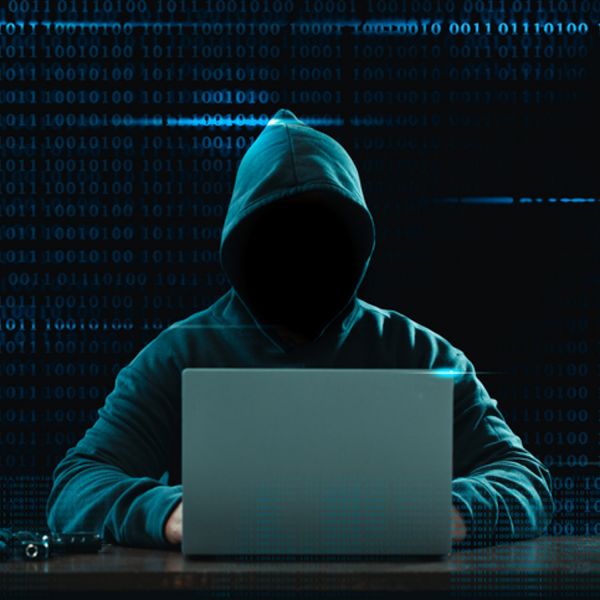 faceless person wearing a hood, at a computer 