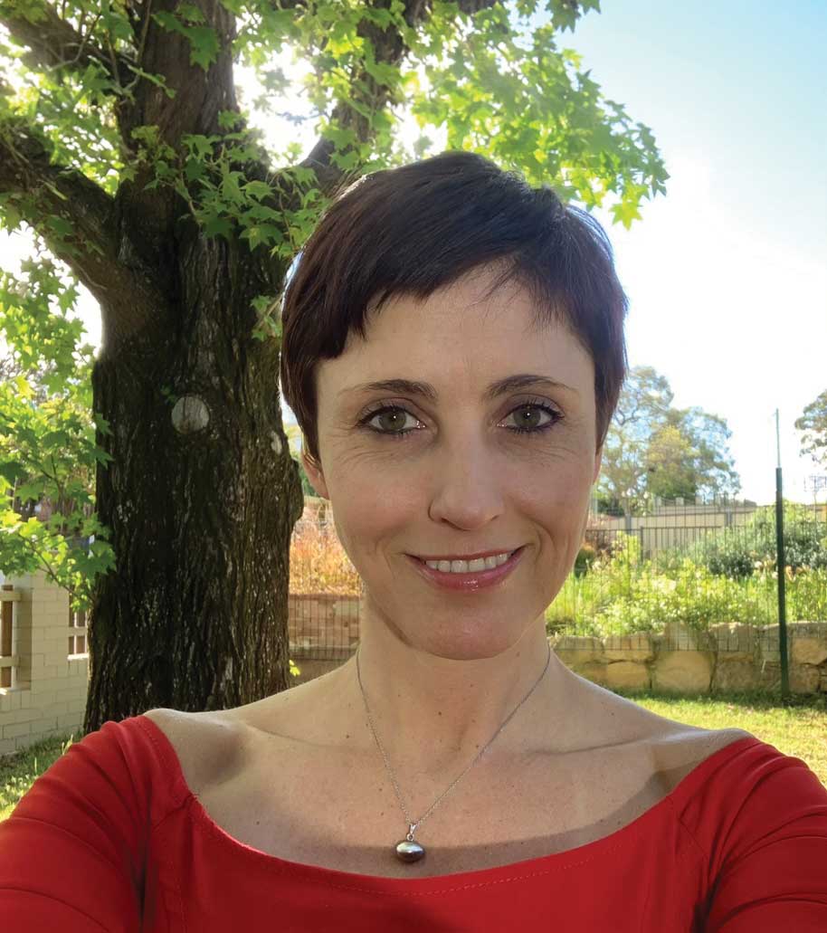 Woman smiling at camera, outdoors with a tree behind