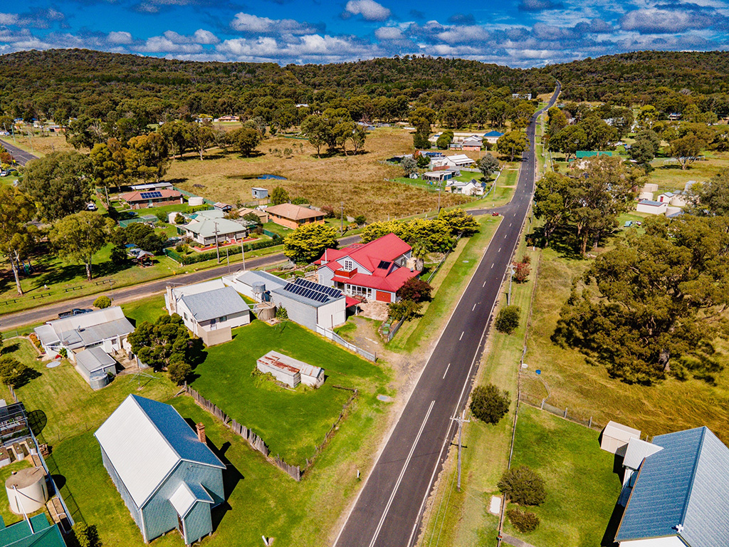Aerial photo shows a regional town. A road cuts through the middle of the picture with houses on either side.One house with a red roof