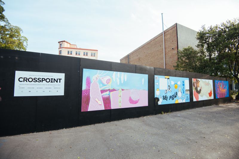 Wide shot of 4 murals painted along a black wall