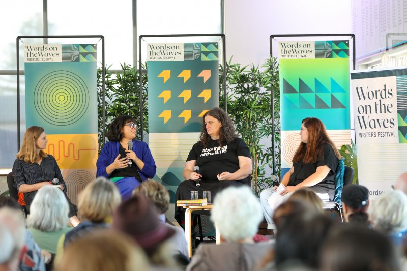 A four person panel with microphones sitting down on stage, with one person talking
