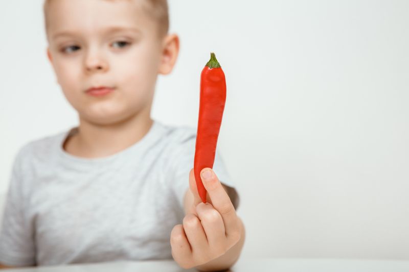 Young boy in white shirt holding up a chilli