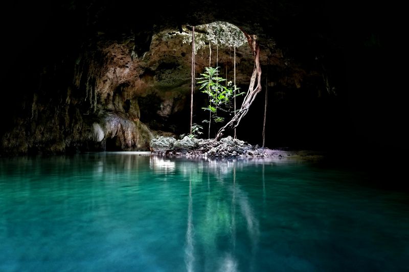 The inside of a sinkhole in Mexico, with light streaming in from the ceiling and water on the ground