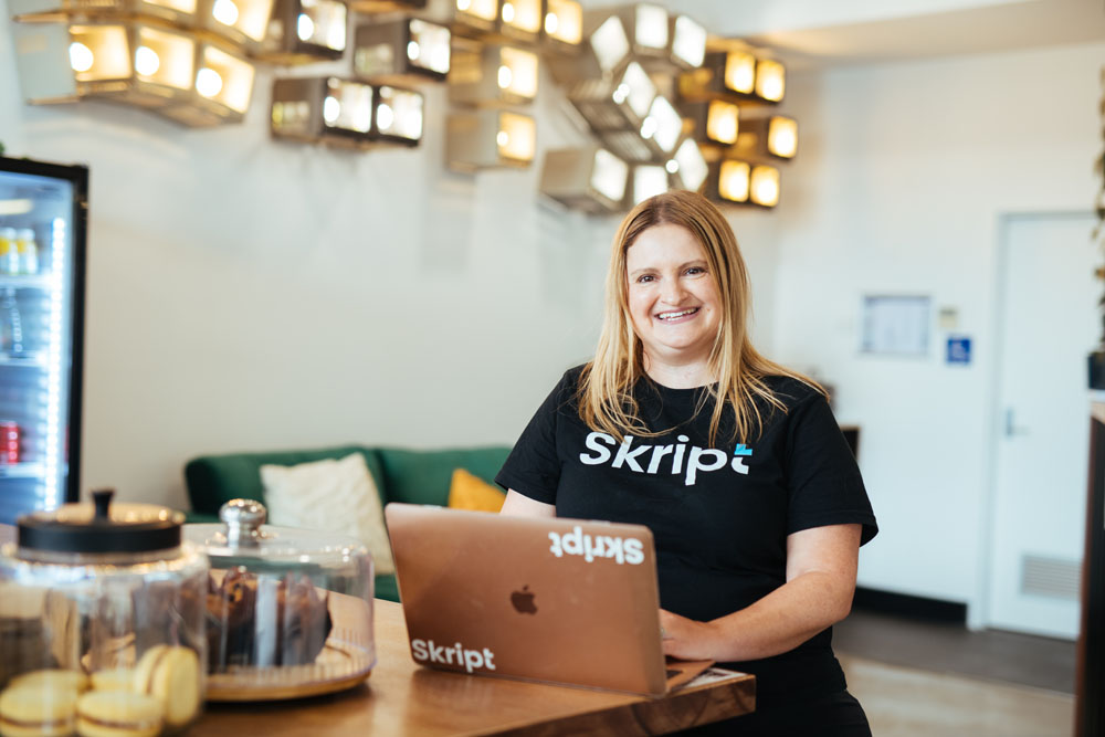 A woman sitting at a table with a laptop smiling