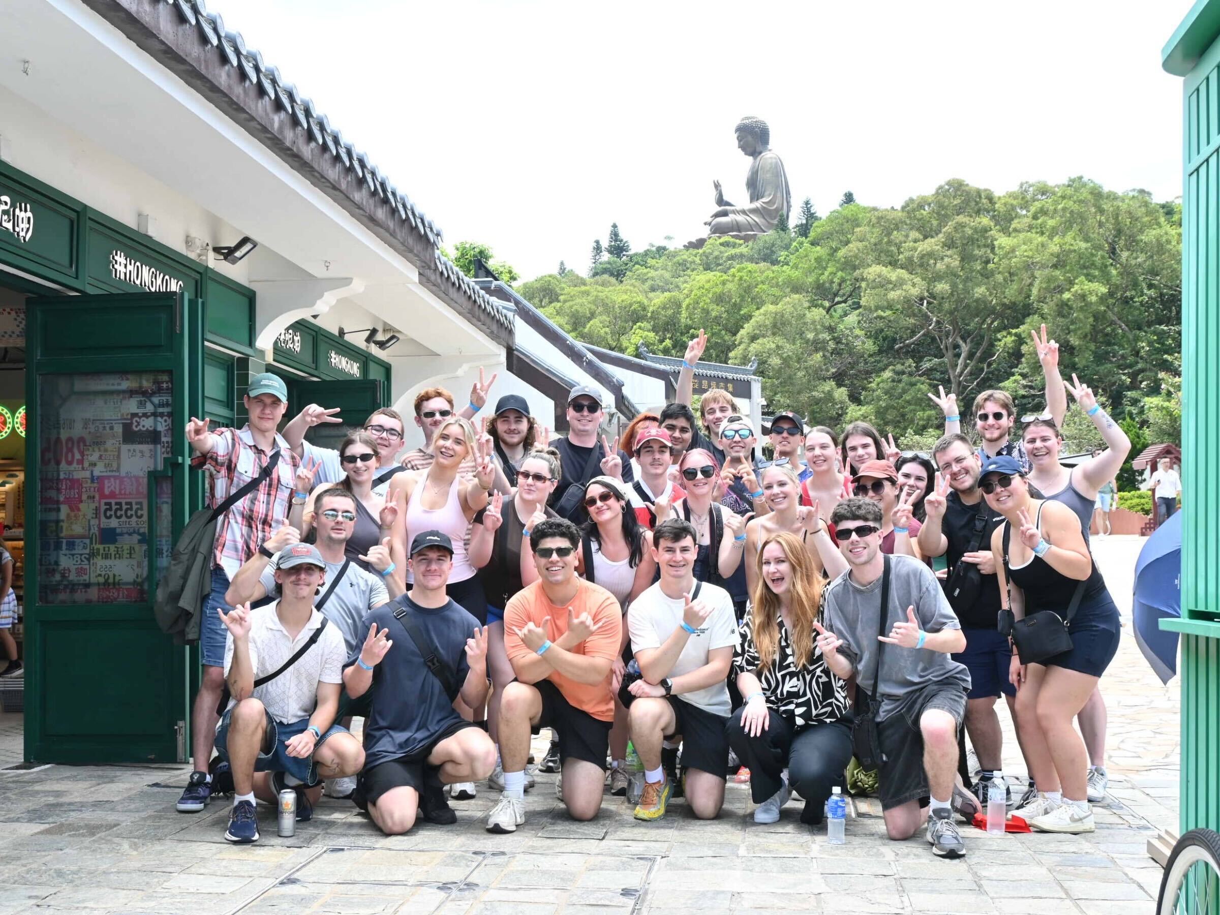 A group of people smily with green hills and the Big Buddha statue in the background