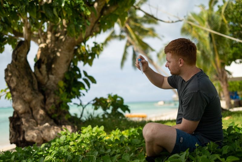 Young man sitting on ground holding up and looking at a test tube