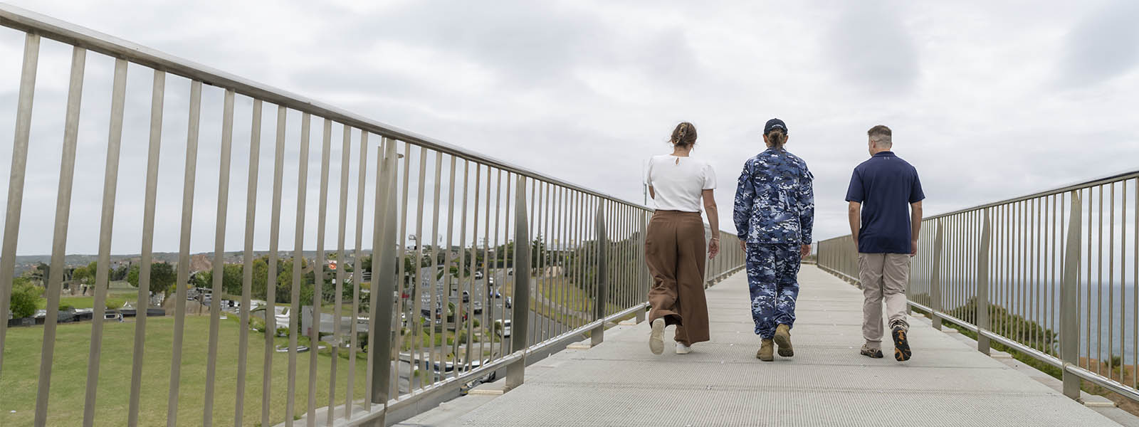 Three people walking away from the camera along the Anzac Bridge