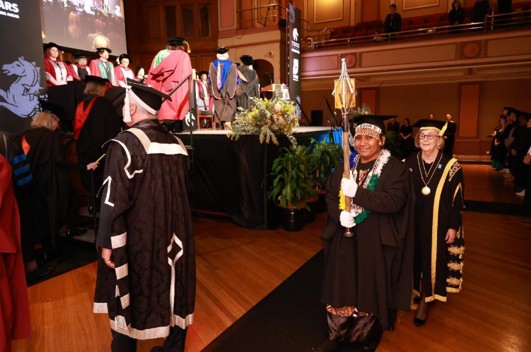 Woman walking towards the graduation stage carrying the mace.