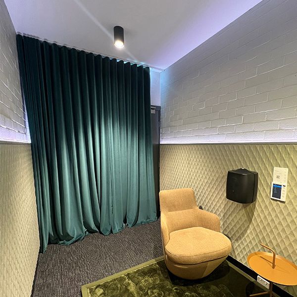 A brown lounge chair is on top of a green rug. A small brown table is in front of the chair. A green curtain covers the back wall.