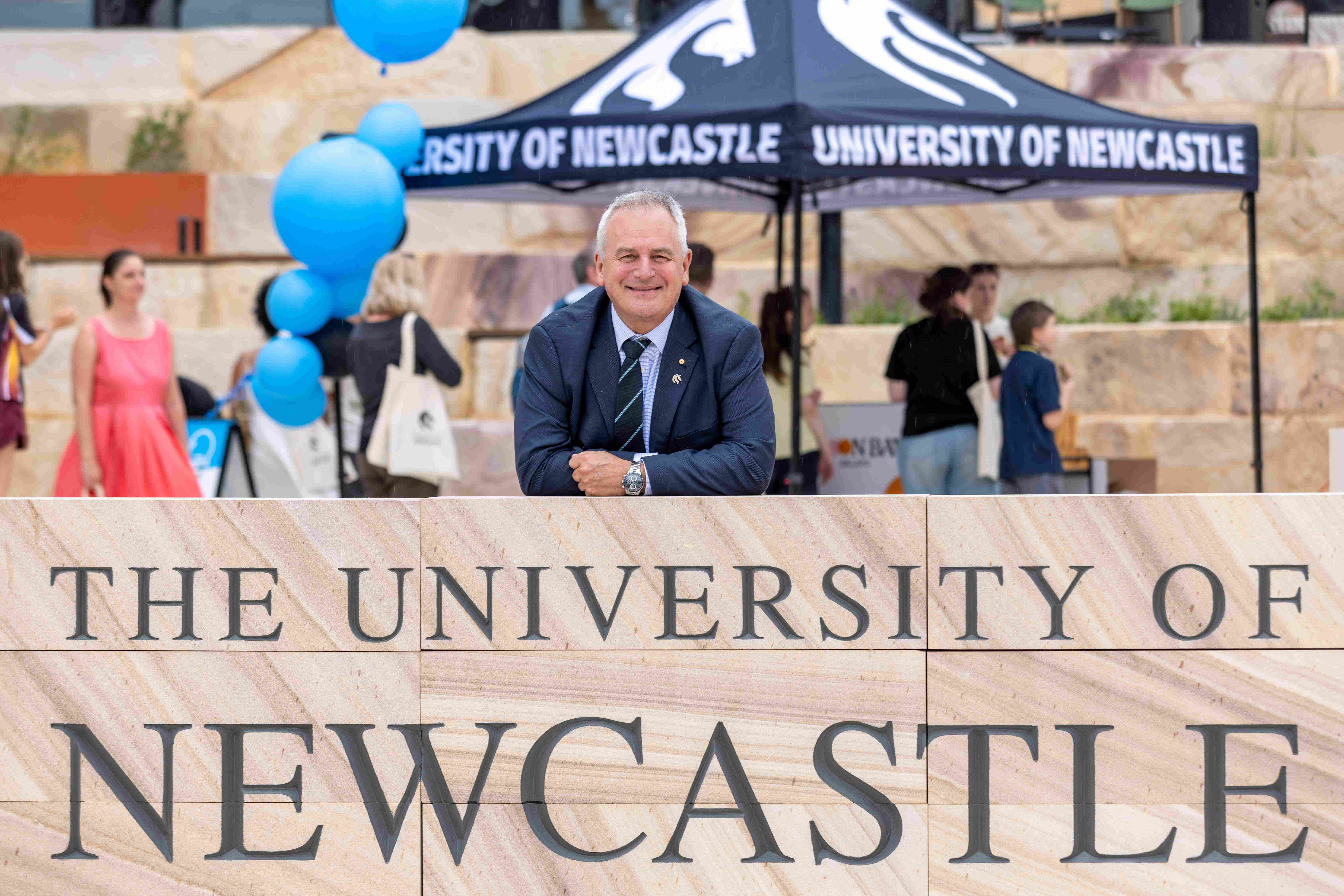 VC Alex Zelinsky stands in front of a university sign and Gosford Central