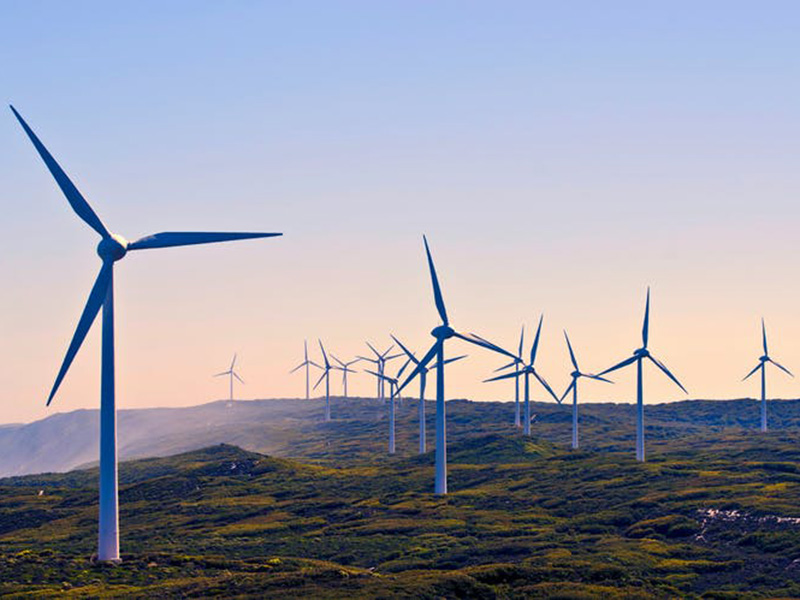 Wide shot featuring wind turbines against hilly terrain and sunset 