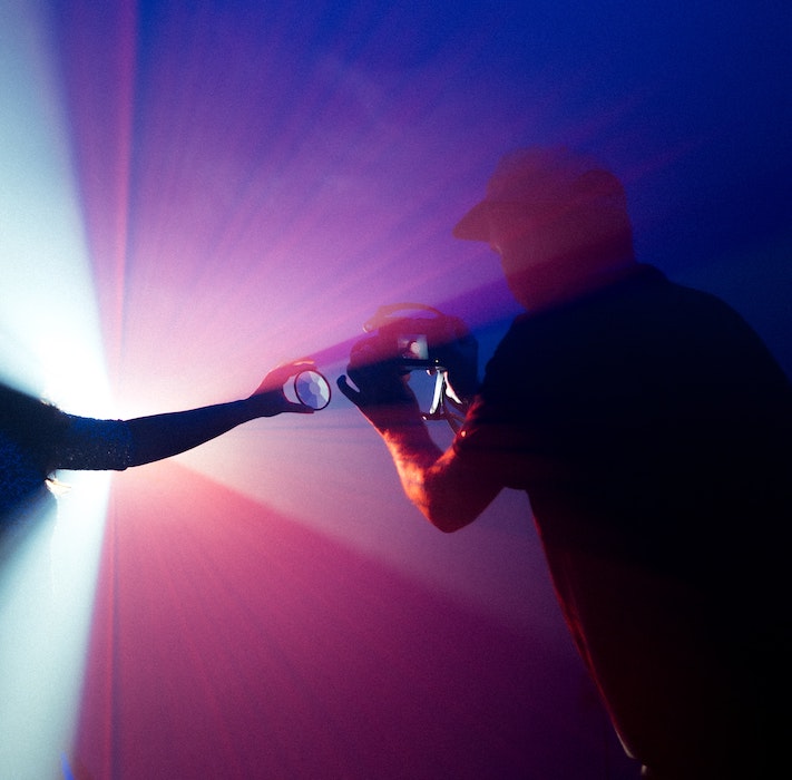 Man wearing a hat taking a photo of colourful lights in a dark room
