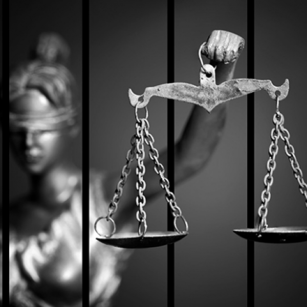 Black and white image of justice scales with a statute holding the scales behind bars. 