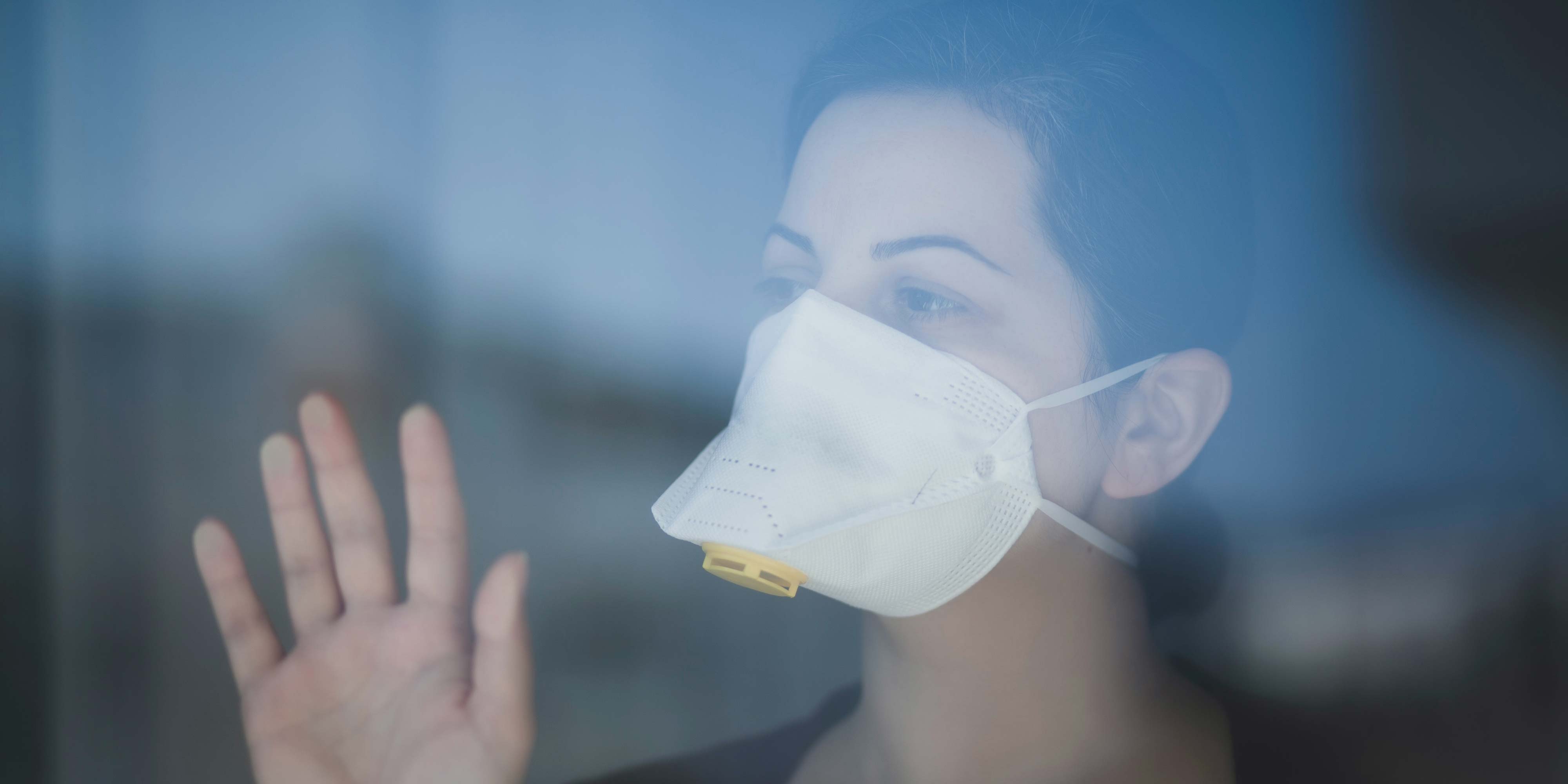 A woman wearing a mask, standing behind a window