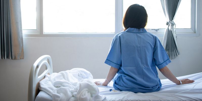 A person sitting on a hospital bed, looking out toward the window.