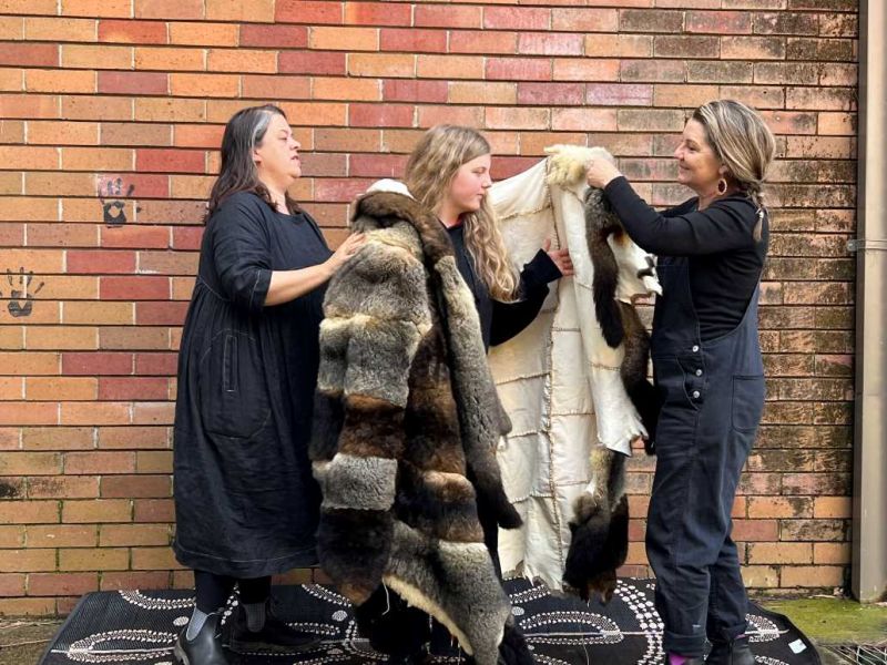 Two adults wrapping a high school student in a possum skin cloak