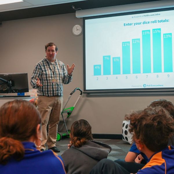 Man standing in front of smart screen and teaching children. UNI STEPS – Connecting students and communities with higher education