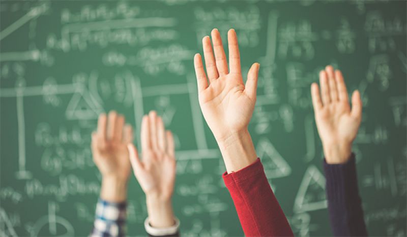 Four hands in the air in a classroom with a blackboard behind them.