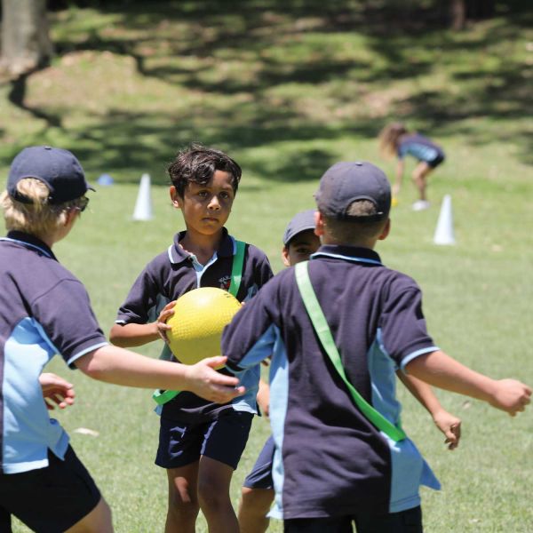 Four primary school children playing games with a ball on an oval