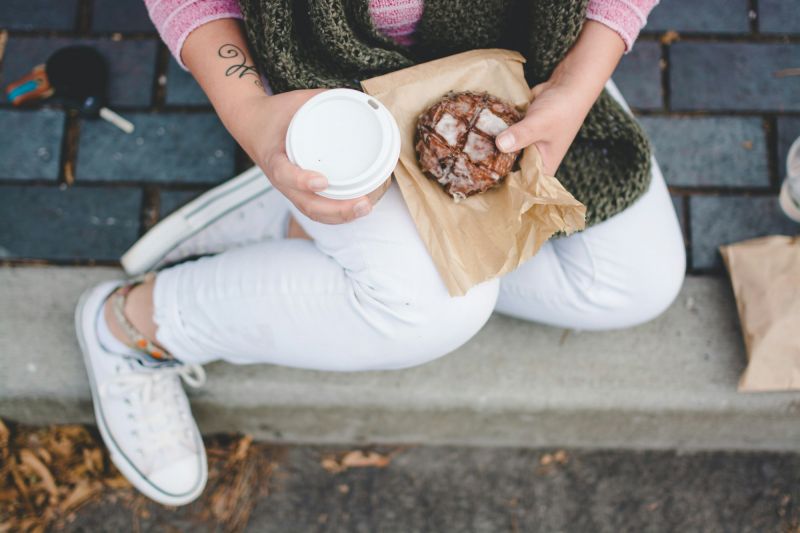 Person sitting on the sidewalk with a coffee and pastry