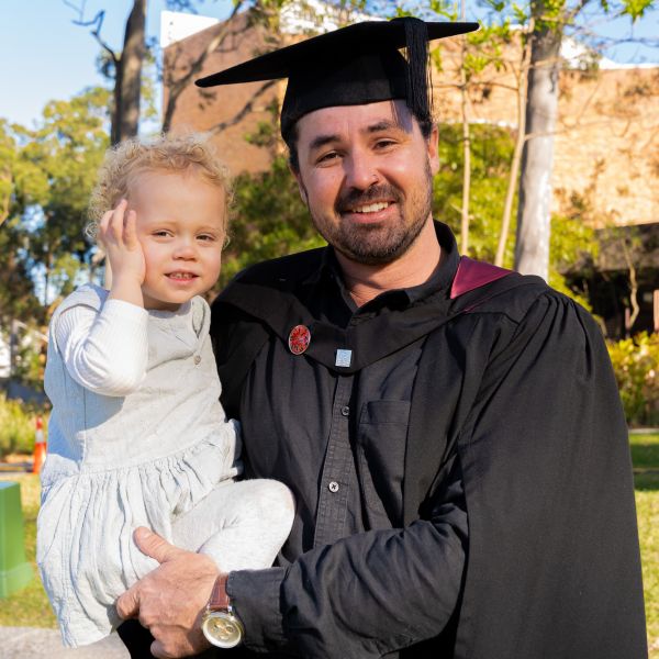 Brendan in his graduation gown holding his daughter . Brendan constructs new life path after government career.