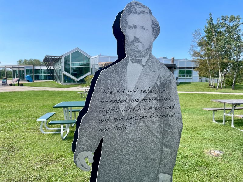 Large 3D black and white art cutout of a man in a suit. There is black text on his body that says
