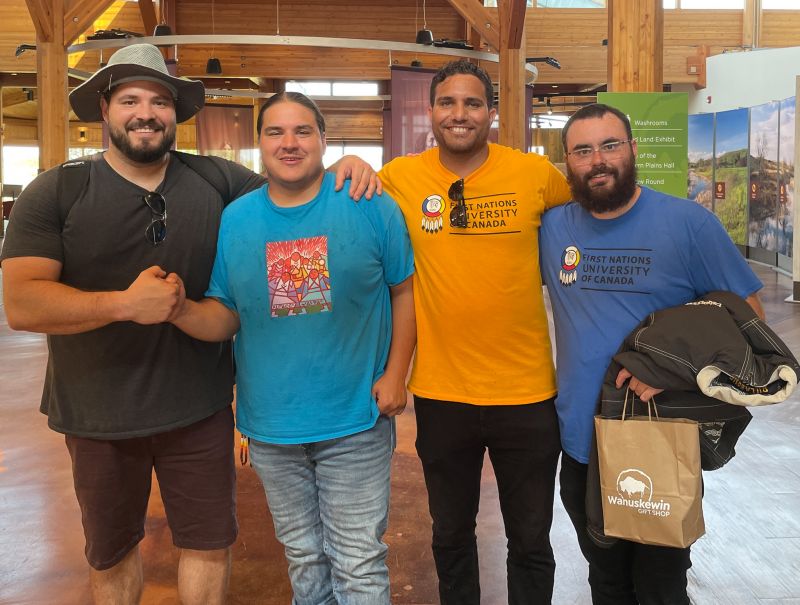 Four men standing in a row in a wooden building with banners in the background.