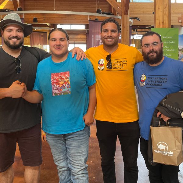Four men standing in a row in a wooden building with banners in the background.
