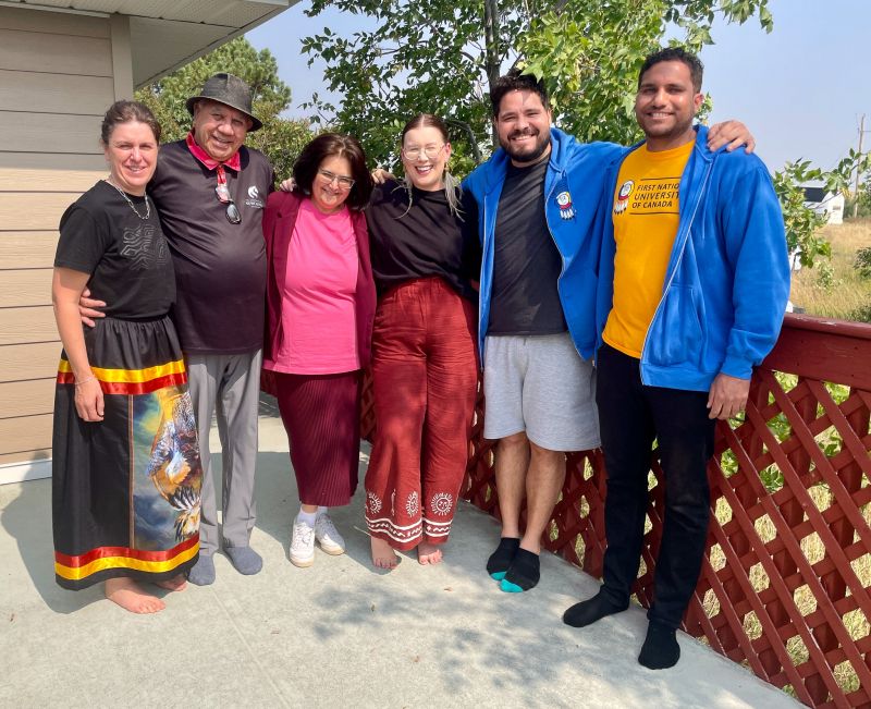 Six people standing in a row on a concrete porch.