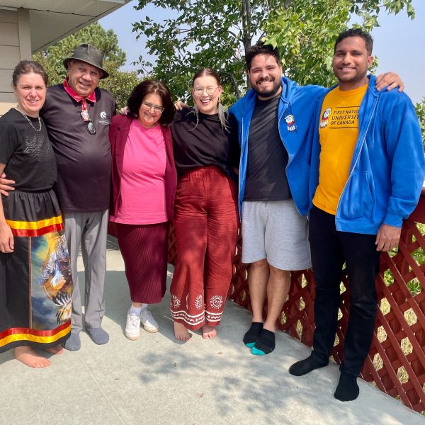 Six people standing in a row on a concrete porch.