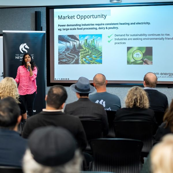 A person presents at the front of a room with a powerpoint slide to a crowd of people. The University of Newcastle and I2N: Pioneering a greener future through innovation.