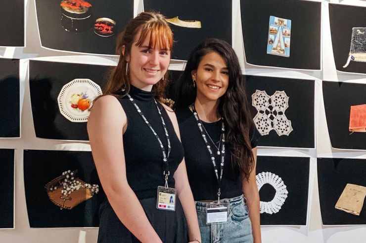 Two female students standing in front of an exhibition wall
