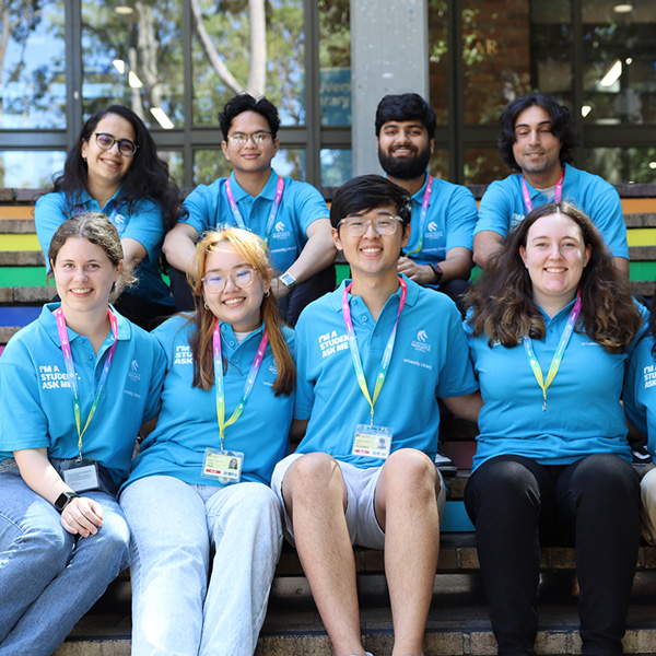 A group of Students Peer Support Assistance (SPSAs) with smiles, sitting on the stairs in front of the Auchmuty Library